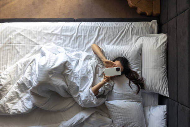 istock Young woman lying in bed and using a smartphone, top view. 2161194548