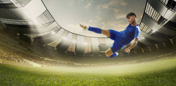 istock Horizontal banner with young athletic man in blue uniform, soccer player hitting ball in a jumper green grass field during match. 3D render of stadium 2161202603