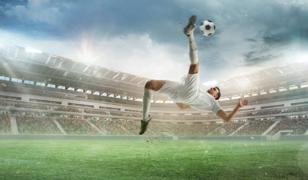 istock Dynamic image of competitive man in white uniform, soccer player during intense match, hitting ball with leg and falling down. 3D render of open air stadium 2161202616