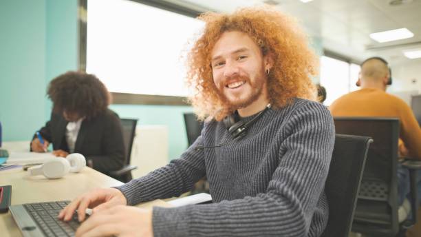 istock Curly-haired office worker smiling at his desk in a bustling workspace. 2161204219