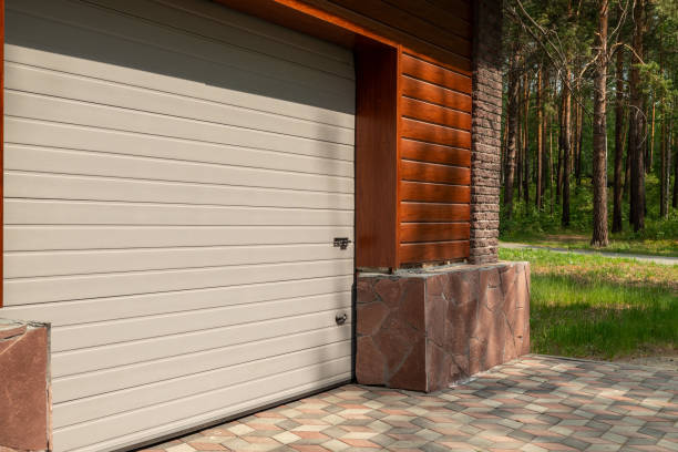 istock Light-colored garage door with a modern design and a brown brick wall with trees in the background 2161205682
