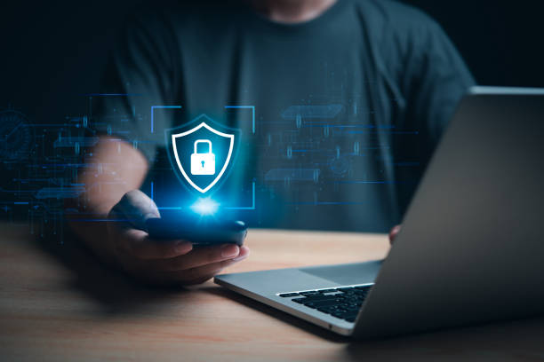 istock Hand holding smartphone with cybersecurity hologram, laptop in background. Represents data protection and digital security. Great for tech firms, cybersecurity awareness, and online privacy. 2161206139