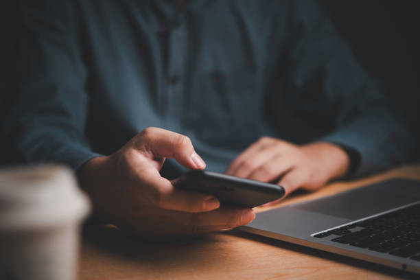 istock Businessman using smartphone at desk, laptop nearby. Represents digital communication, multitasking. Ideal for tech, corporate themes. 2161206185