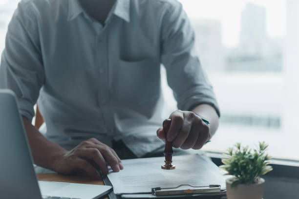 Businessman stamping documents at office desk, symbolizing approval, authorization. Suitable for legal, administrative, business themes. Represents formality, professionalism.