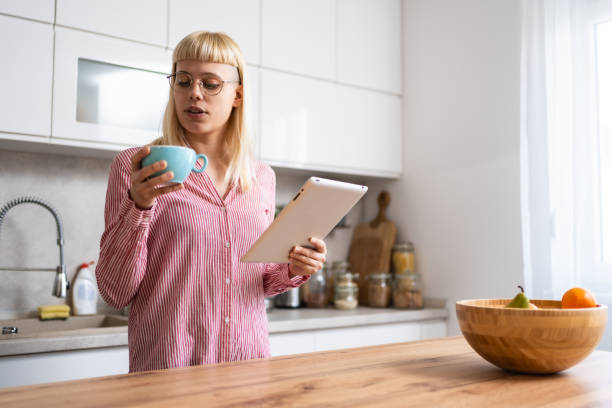 istock Young businesswoman real estate agent morning routine, drinking coffee in kitchen using digital tablet to read emails. Working at home female professional designer, business owner, confident lifestyle 2161211066
