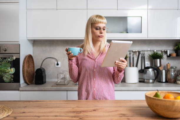 istock Young businesswoman real estate agent morning routine, drinking coffee in kitchen using digital tablet to read emails. Working at home female professional designer, business owner, confident lifestyle 2161211074