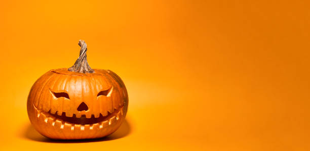 Carved Halloween pumpkin as Jack-o'-lantern over orange background with copy space