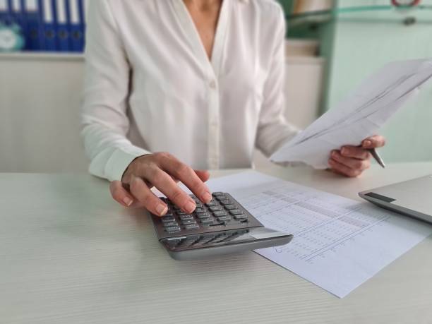 istock Close Up of a Woman's Hand Using a Calculator While Reviewing Documents in an Office 2161216491