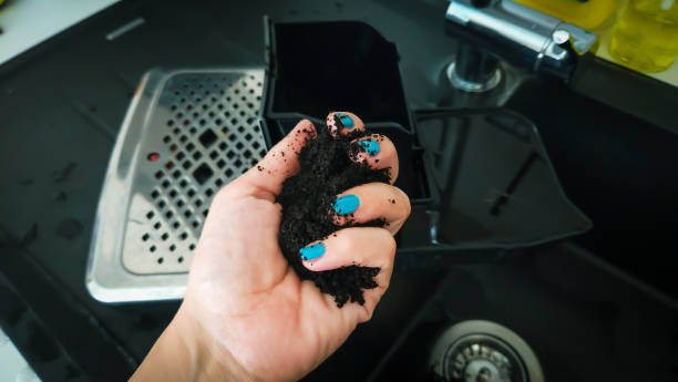 A hand with blue nail polish holds the leftover coffee grounds from the coffee machine