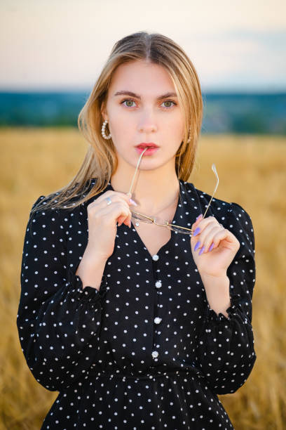 Blonde woman in a black dress poses in a wheat field.