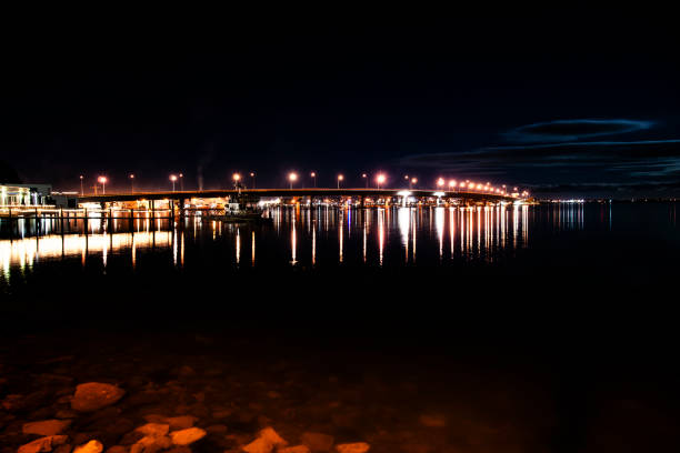 Tauranga Harbour Bridge illuminated at night with lights reflecting in water below.