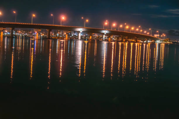 Tauranga Harbour Bridge illuminated at night with lights reflecting in water below.