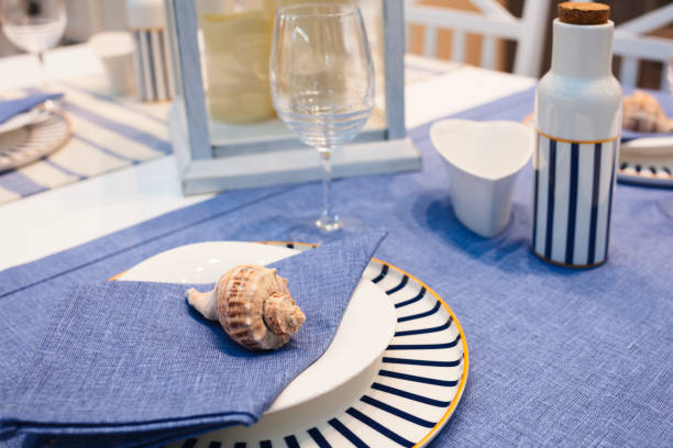 istock A table with a blue and white striped tablecloth and a shell on a napkin. The table is set for a meal with a wine glass and a bottle 2161230961