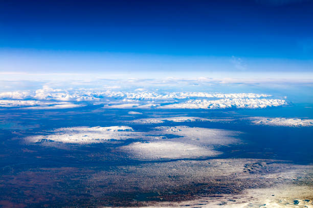 An expansive aerial view of Iceland from 30,000 feet, showcasing the country's rugged landscape. Snow-covered mountains and glaciers are visible under a clear blue sky, with the coastline extending into the distance. The image captures the stark beauty and vastness of Iceland's terrain, highlighting its unique geographical features.