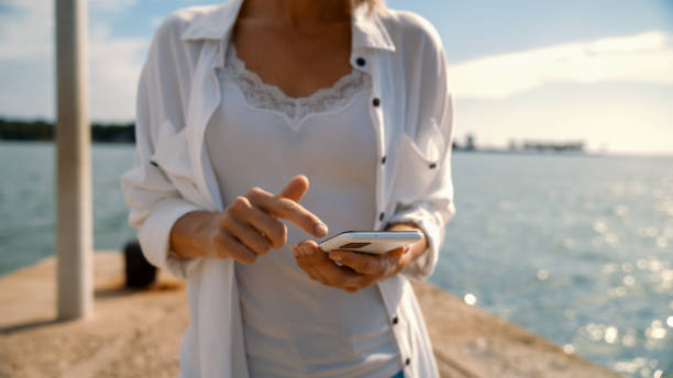 istock Caucasian Woman Tapping on Smarphone at Oceanfront 2161231481