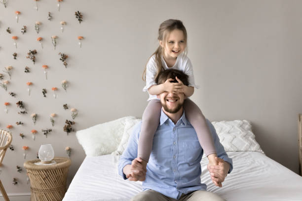 istock Kid closing fathers eyes with palms, sitting on his shoulders 2161233152
