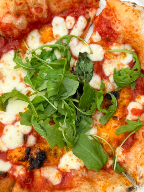 Full frame image of whole, freshly baked takeaway Margherita pizza, stringy, melted buffalo mozzarella cheese, rich tomato marinara sauce topping, garnished with rocket leaves, elevated view