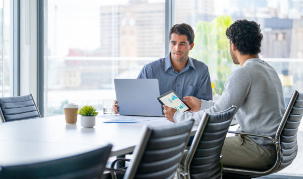 istock Two businessmen working on a digital tablet and laptop computer in the office a board room or meeting room. 2161243413