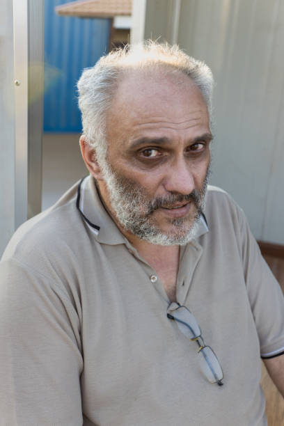 single old man with a beard and gray hair sitting outdoors , half portrait