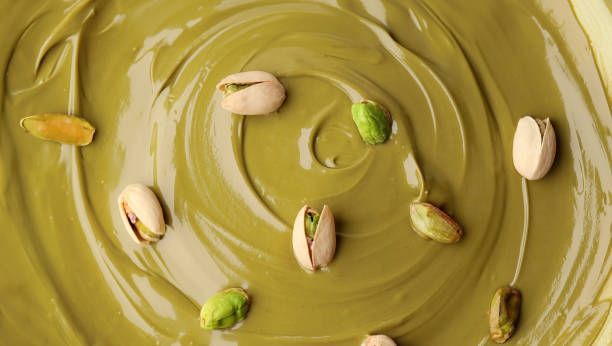 Green pistachio paste with pistachio nuts in a shell. Pistachio cream. green background