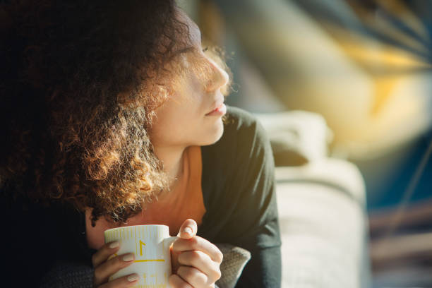 istock Young woman relaxing on sofa at home drinking coffee and looking 2161267598