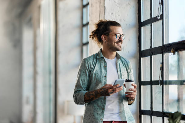 Happy freelancer using cell phone on coffee break by the window.