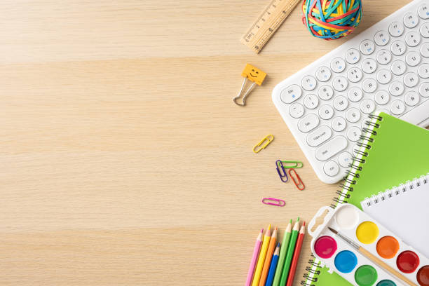 istock Assorted school supplies including a keyboard, notebooks, pencils, and watercolor paints on a wooden desk 2161286587