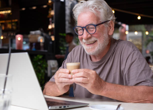 istock An elderly man enjoying a coffee and pastry in a cafe, smiles while using his laptop on a video call. Cheerful senior male, highlighting happiness and contentment in a relaxed atmosphere 2161288717