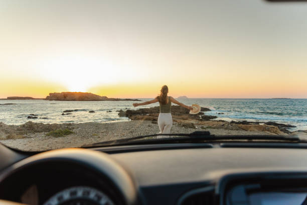 Young woman taking a break from driving a car. She is enjoying the sunset and looking at the view. Freedom concept