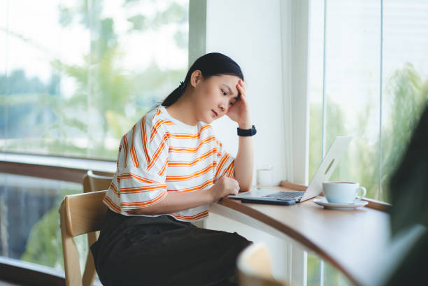 istock Asian woman using laptop sitting at coffee shop, feels concerned thinking about work. 2161295766