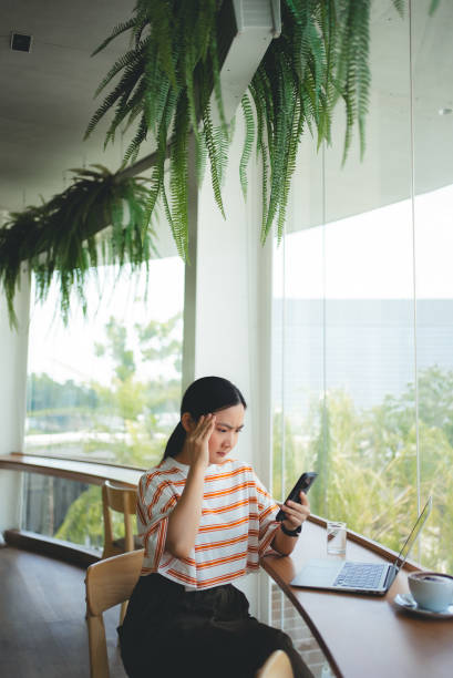 istock Asian woman sitting at coffee shop looking at smartphone screen and having problem. 2161296029