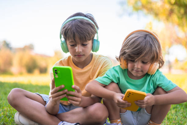 istock Two Children Having Fun Together Outdoors Using A Mobile Phone And Headphones Playing Online Video Games Or Watching Entertainment Videos. Streaming 2161297668