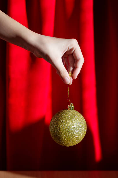 Close-up of child's hand holding golden Christmas ornament against red background