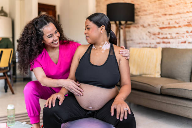 istock Young pregnant doing physical therapy using ball with physiotherapist at house call 2161313576