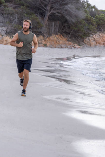 istock Morning Routine: Man Running Alone Along the Shoreline with Headphones 2161313677