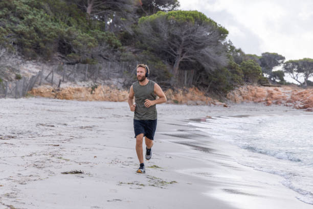 istock Morning Routine: Man Running Alone Along the Shoreline with Headphones 2161314264