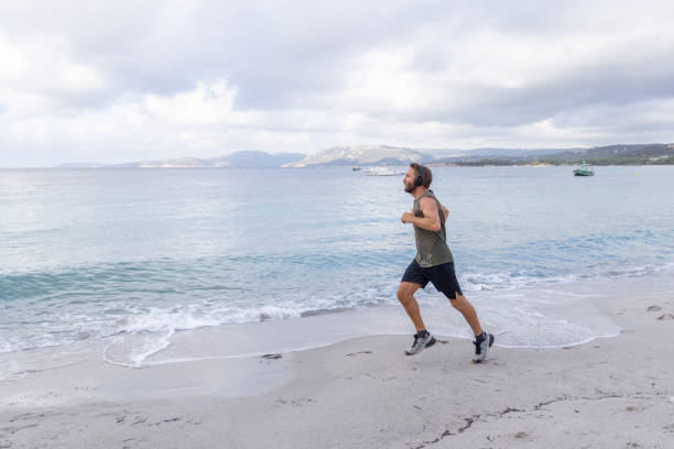 istock Morning Routine: Man Running Alone Along the Shoreline with Headphones 2161315635
