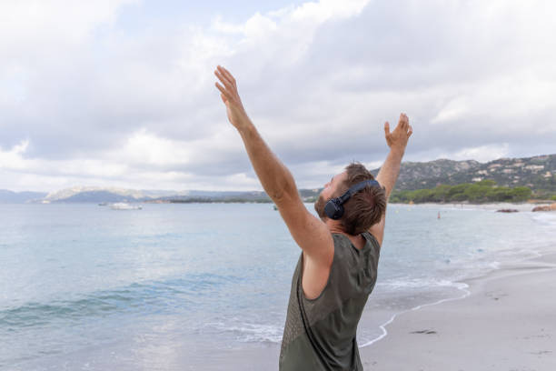 istock Man with Headphones Raising Arms on Beach 2161317496