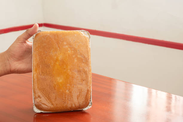 Packaged mantecada. A hand holding a plastic coated corn mantecada inside an aluminum tray on a wooden table. Sponge cake. Take away food. Image with copy space.