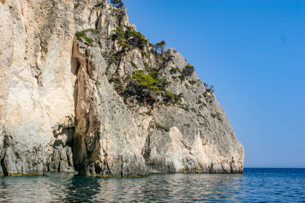 Zakynthos, Greece - Ausgust 1st 2005 - A cliff on Zakynthos island, covered with sparse vegetation, rising sharply from the clear blue sea under a bright sky.