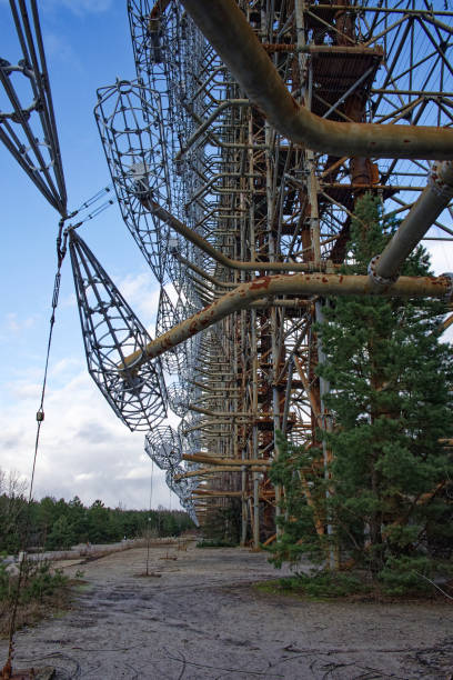 The complex metallic structure under a blue sky with white clouds, surrounded by dry vegetation. Duga is a Soviet over-the-horizon radar station for an early detection system for ICBM launches. la compleja estructura metálica bajo un cielo azul con nubes blancas, rodeada de vegetación seca. duga es una estación de radar soviética sobre el horizonte para un sistema de detección temprana de lanzamientos de misiles balísticos intercontinentale