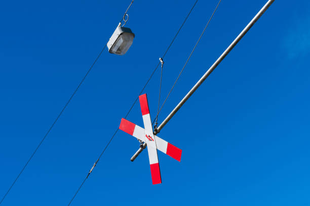 A red and white railroad crossing signal hangs from a metal pole against a bright blue sky.