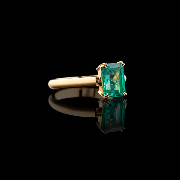 Beautiful yellow gold ring with diamonds and emerald on a black background