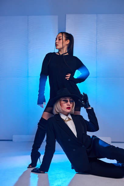 istock Graceful Ladies In Black Outfit Posing At Camera While Dancing In Studio On Blue Background 2161357468