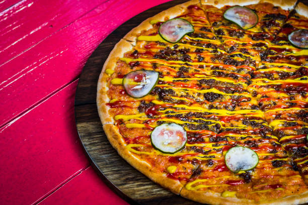 Pizza with Vine-ripened tomato sauce as the base. Topped with smoked minced beef, Montreal seasoning and a mixture of mozzarella, smoked cheddar and parmesan cheese. Garnishing it off with American mustard, tomato ketchup and house pickles to create a version of a cheese burger. pizza con salsa de tomate madurado en rama como base. cubierto con carne picada ahumada, condimento montreal y una mezcla de mozzarella, queso cheddar ahumado y queso parmesano. adorne con mostaza americana, salsa de tomate y pepinillos de la casa para c