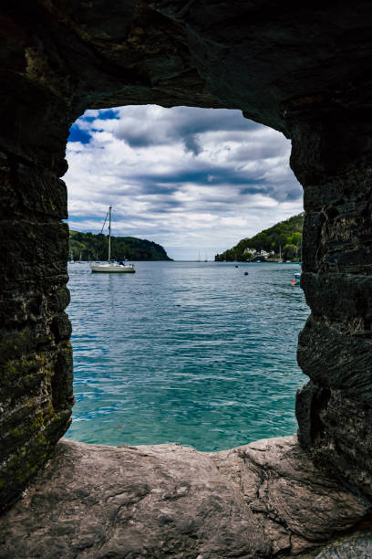 The River Fowey meanders through the charming town in Cornwall, creating a picturesque and tranquil scene. The waterfront is lined with quaint buildings and lush greenery, reflecting beautifully in the calm river waters. Boats gently float on the river, adding to the idyllic and serene atmosphere of this scenic location.