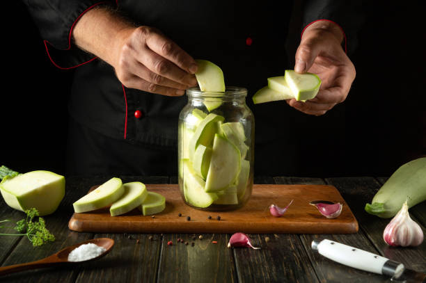 istock Chef hands filling jar with chopped vegetable marrow before canning with spices on kitchen table. Concept of pickling tasty zucchini 2161359601