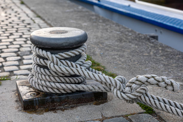 A thick white rope is wrapped around a gray metal bollard, securing a vessel to the dock.