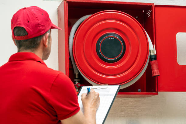 Technician performing periodic inspection of fire hose cabinet. Fire protection systems maintenance for safety.