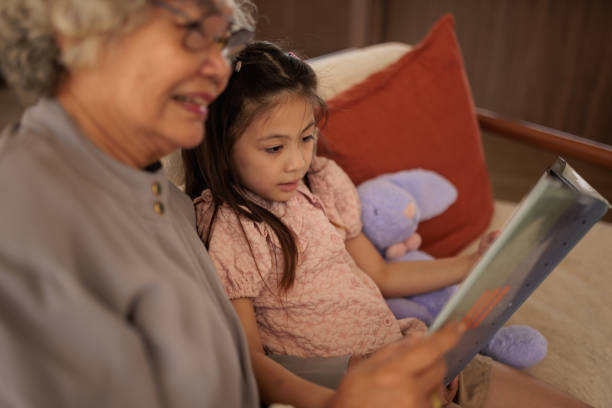 Happy family at home. Two girls sisters twins grandmother reading story book together. Good time at home. Grandma teaching granddaughters reading book fairytale telling story. Family generations